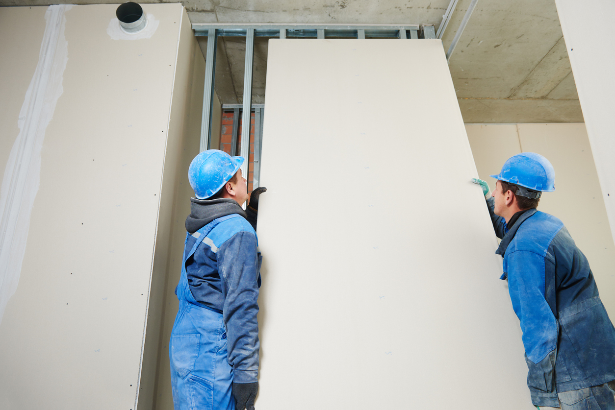 Two drywall contractors installing a panel of drywall