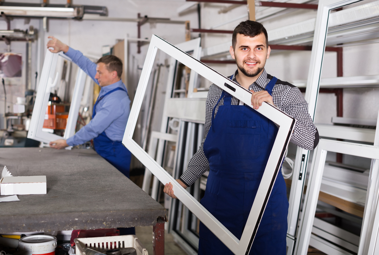 A man holding a replacement window frame for a skylight in a window manufacturing workshop