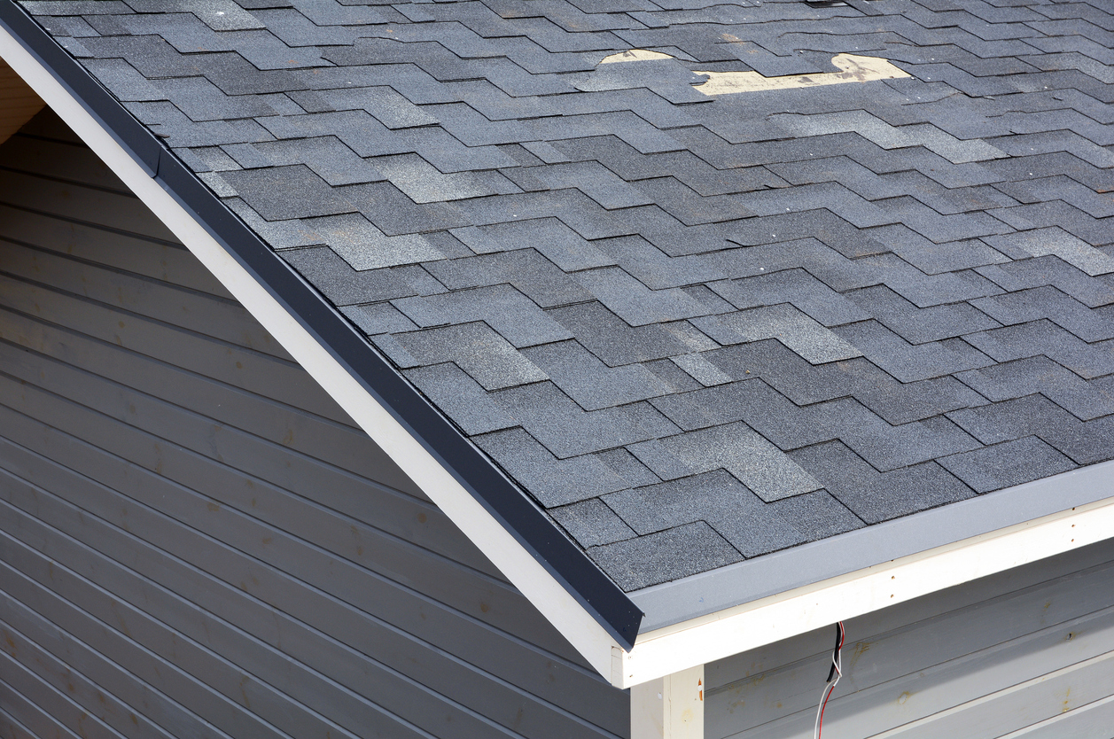 Close up of a t-lock shingle roof with several ripped out shingles needing to be replaced