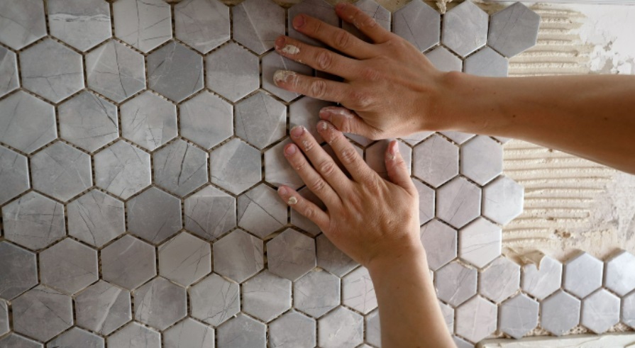 Pressing white, hexagonal, marble tile into place on a wall 